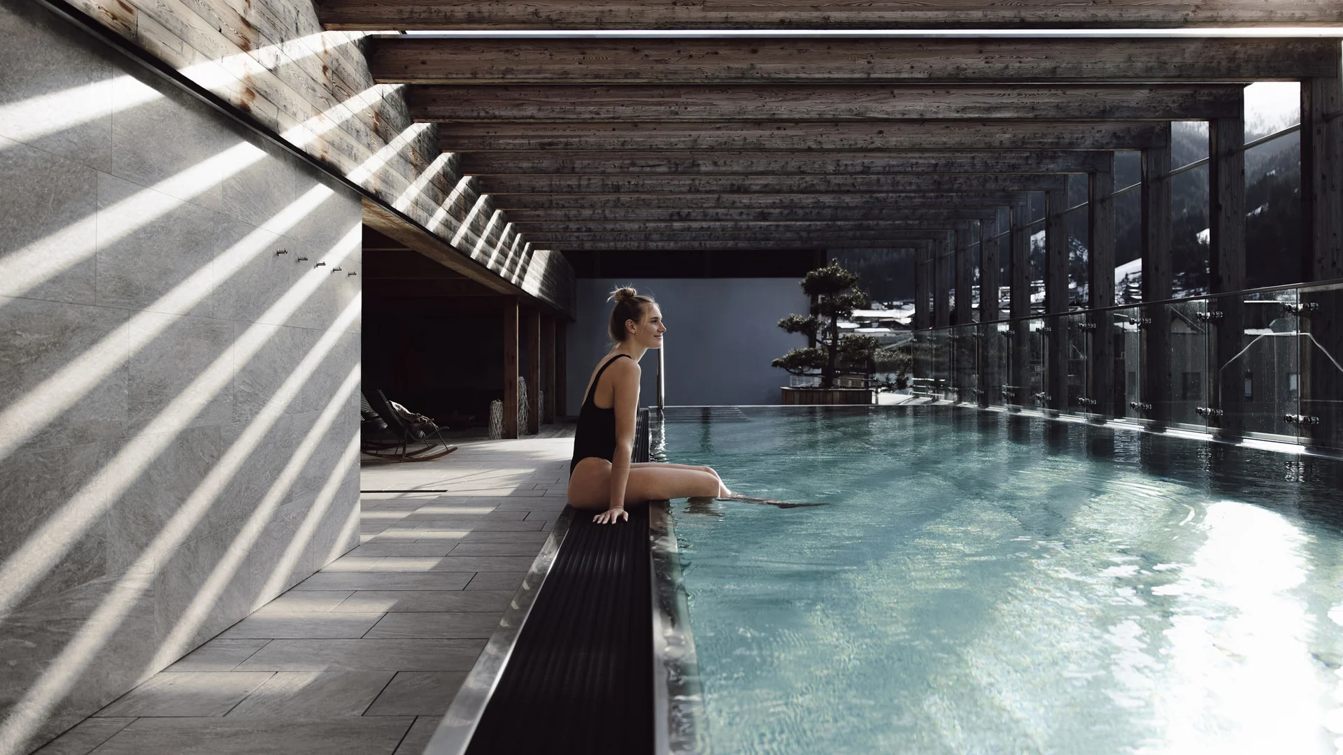 Frau sitzt am Rand eines überdachten Pools mit Bergblick