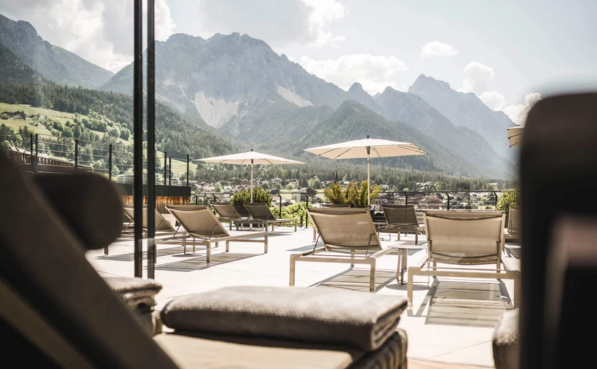 Excelsior Dolomites Life Resort ****S © Hannes Niederkofler Liegestühle und Sonnenschirme mit Bergblick an einem sonnigen Tag