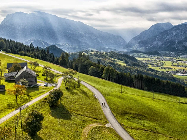 Landschaft mit Berg, grünen Feldern und zwei Radfahrern auf der Straße