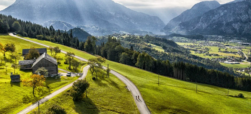 Landschaft mit Berg, grünen Feldern und zwei Radfahrern auf der Straße