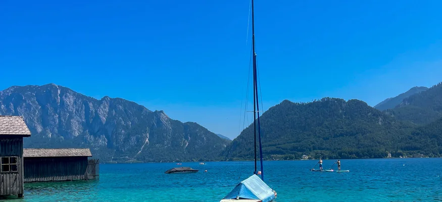 Segelboot auf klarem See vor Bergen bei sonnigem Himmel