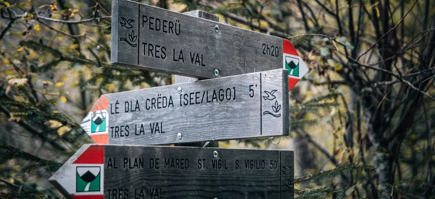 Holzwegweiser in einem bewaldeten Gebiet mit Wanderzeiten zu verschiedenen Zielen