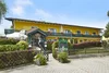 Yellow hotel with green entrance and flowers on the balcony