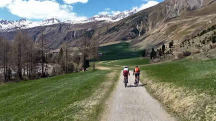 Zwei Radfahrer auf einem Weg in einer Berglandschaft mit schneebedeckten Gipfeln