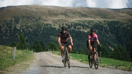 Gravel Badges © Nicola Littmann Zwei Radfahrer fahren auf einem Bergweg mit Hügeln im Hintergrund