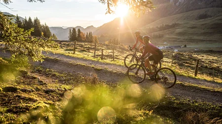 Zwei Radfahrer fahren auf einem Waldweg bei Sonnenuntergang in den Bergen