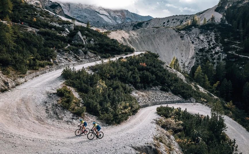 Zwei Radfahrer auf einer kurvigen Bergstraße in einer alpinen Landschaft