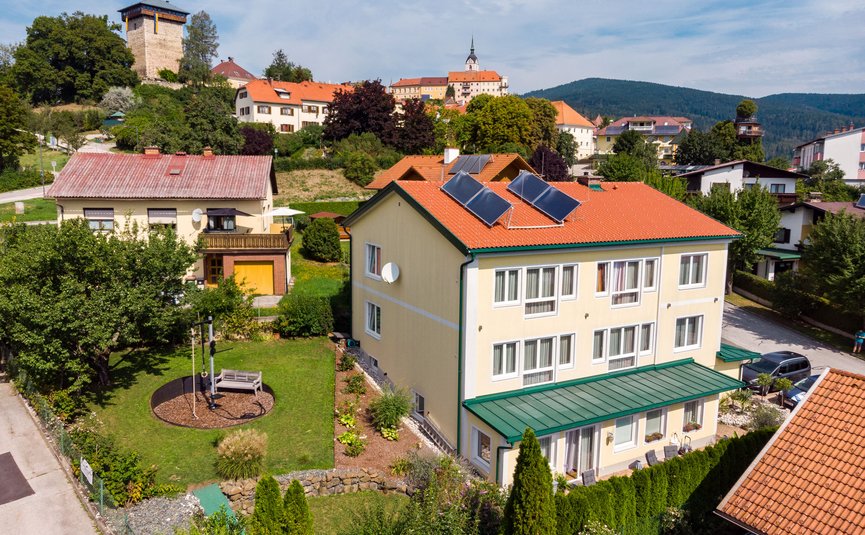 Dorf mit Häusern, Solarpanelen und Burgturm im Hintergrund bei klarem Himmel