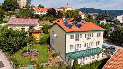 Village with houses, solar panels, and castle tower in background under clear sky