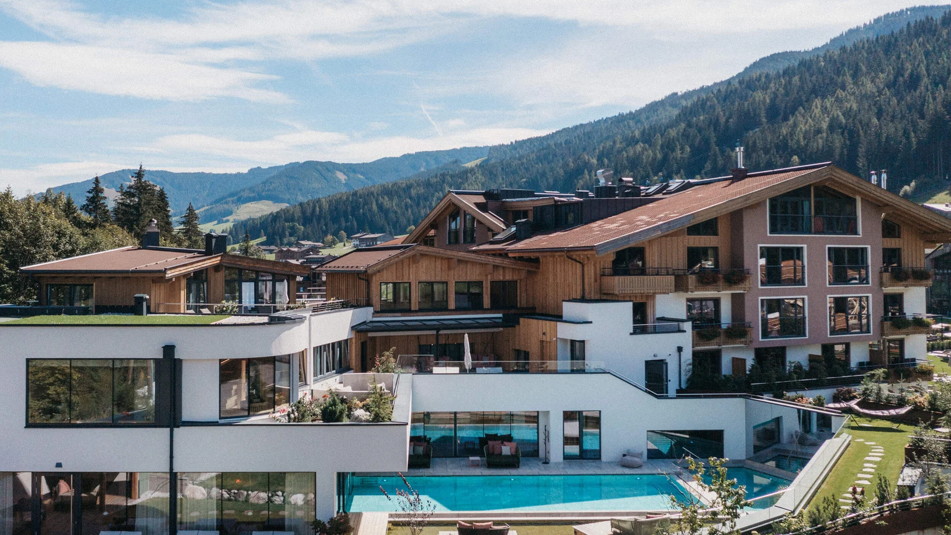 Moderne Villa mit Pool vor bewaldeten Bergen und blauem Himmel