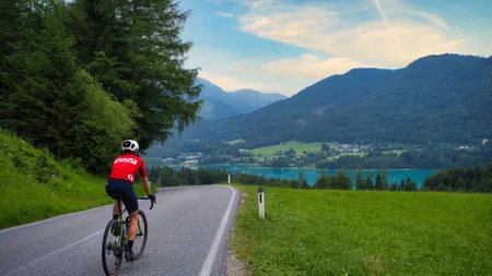 Drei Seen, eine Gravelrunde: Die 3-Seen-Tour ab Fuschl © Fuschlsee Tourismus - GravGrav Radfahrer auf Bergstraße mit See und Bergen im Hintergrund