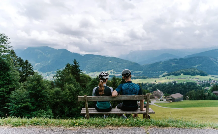 Two cyclists sitting on a bench overlooking mountains and valley