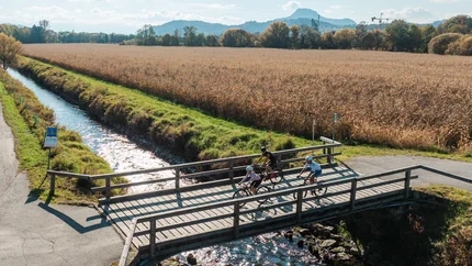 Three cyclists crossing a bridge over a stream in rural fields