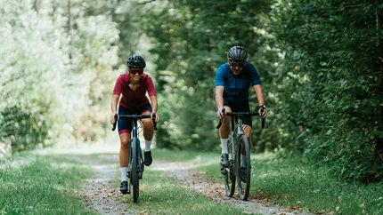 Zwei Fahrradfahrer auf Waldweg umgeben von grünen Bäumen