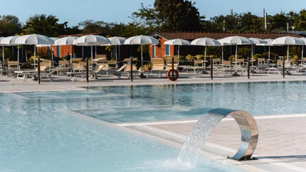 Moderner Pool mit Wasserfontäne und Liegestühlen unter weißen Sonnenschirmen