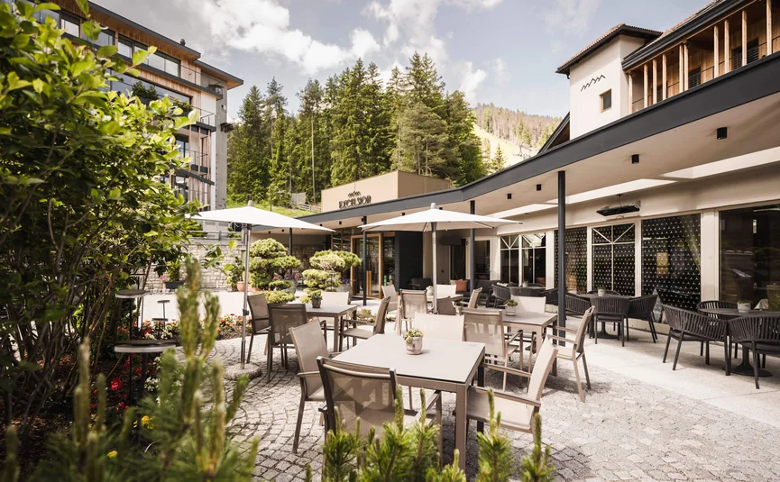 Hotel outdoor seating area with tables, chairs, umbrellas and forest background