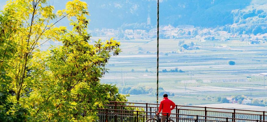 Person mit Fahrrad auf Aussichtspunkt mit Blick auf Tal und Berge