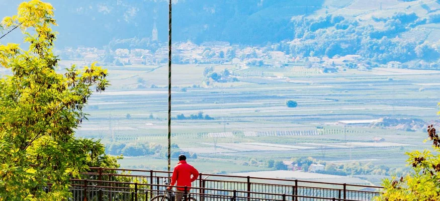 Person mit Fahrrad auf Aussichtspunkt mit Blick auf Tal und Berge