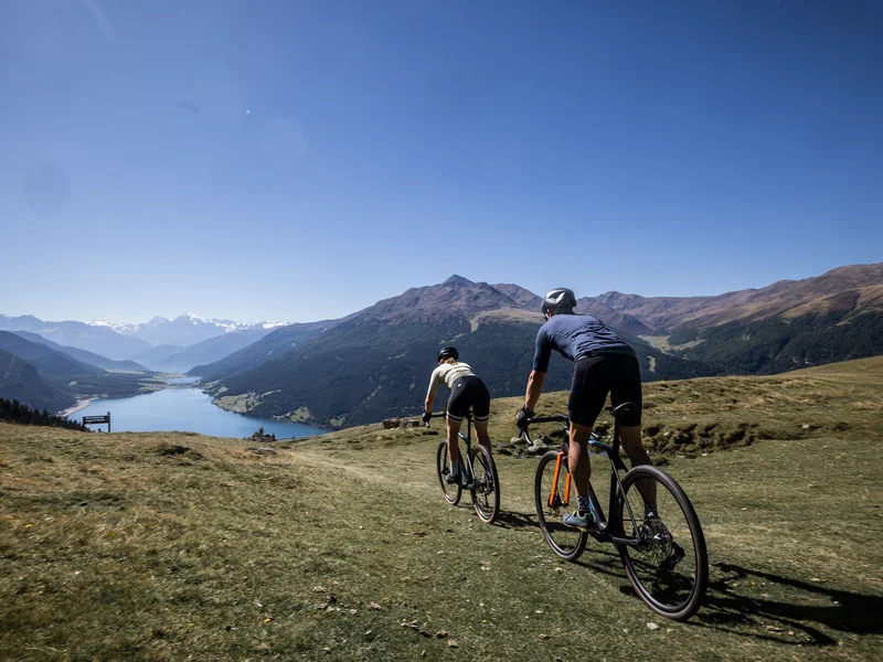 Gravelbike Holidays © Heiko Mandl Zwei Radfahrer fahren auf einem Bergpfad mit Blick auf Tal und Berge