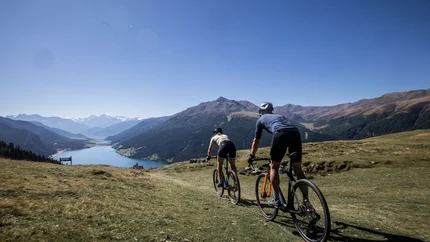 Zwei Radfahrer fahren auf einem Bergpfad mit Blick auf Tal und Berge