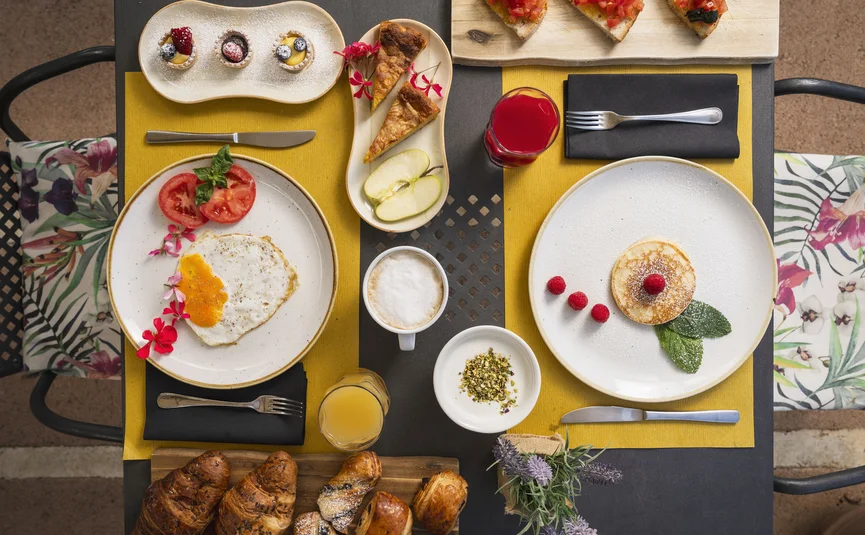 Table with balanced breakfast: eggs, fruit, croissants, coffee, and juice