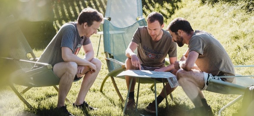 Drei Männer sitzen im Garten und schauen auf eine Karte