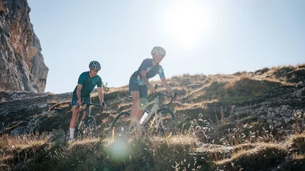 Two cyclists riding on a mountain trail in sunny weather