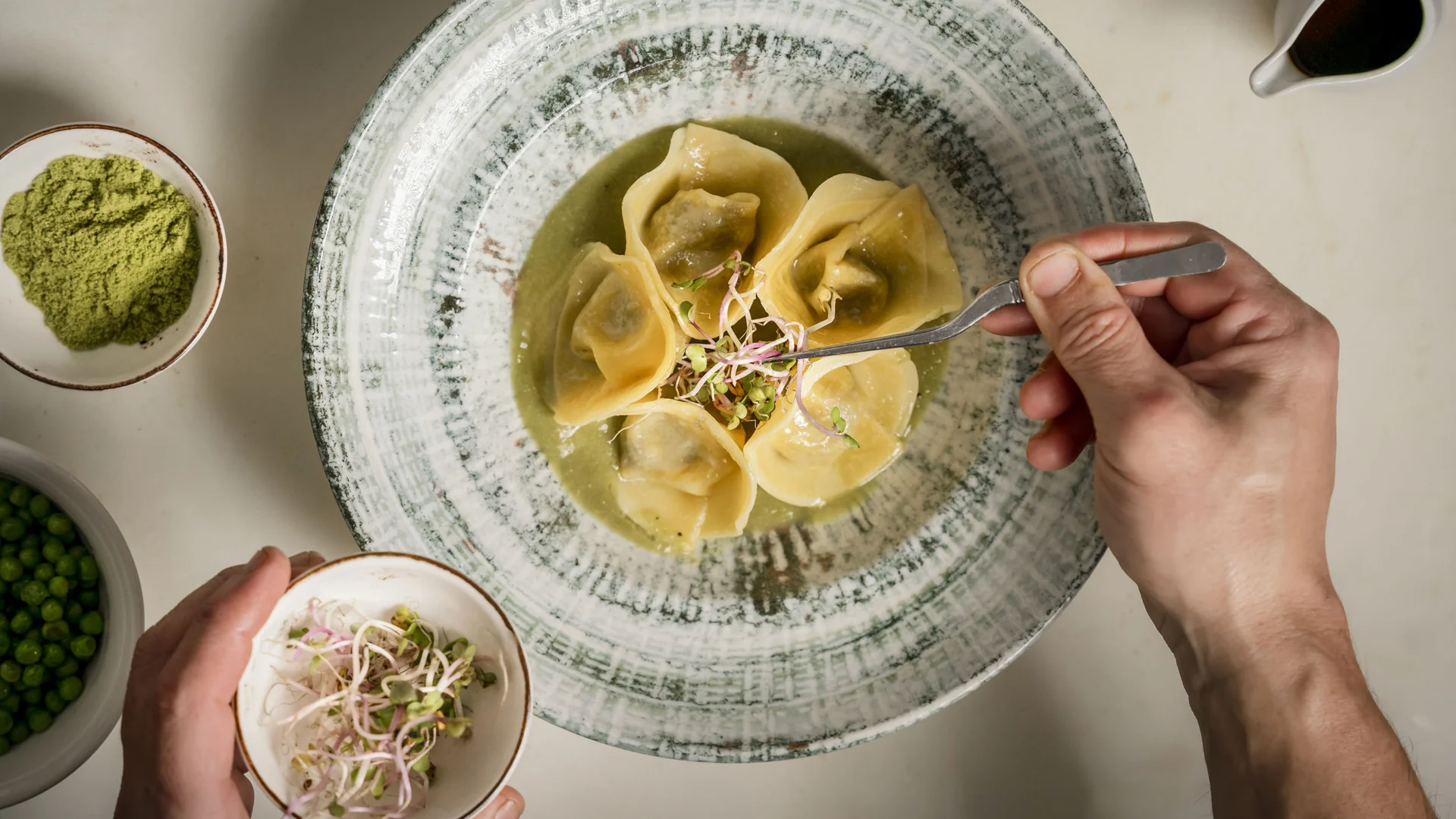 Gravelbiken in der Toskana © Hotel Casolare Le Terre Rosse Eine Hand richtet Ravioli mit Sprossen an, umgeben von grünen Zutaten