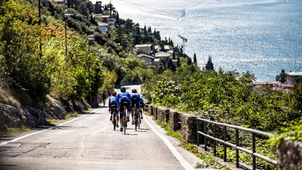 Group of cyclists on road overlooking lake and mountains in background