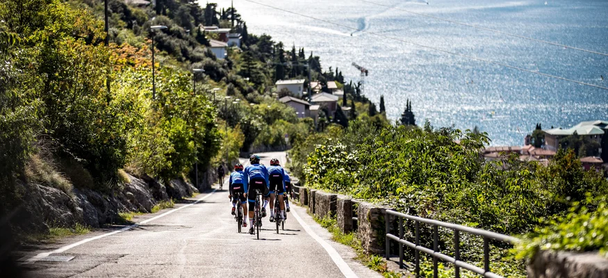 Group of cyclists on road overlooking lake and mountains in background
