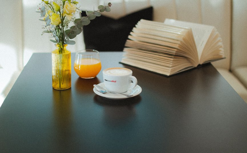 Schwarzer Tisch mit Blumen, Orangensaft, Kaffee und offenem Buch