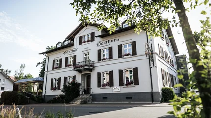 Posthorn Hotel-Restaurant © Dimitri Dell Weißes Gasthaus Posthorn mit dunklen Fensterläden, eingerahmt von Bäumen