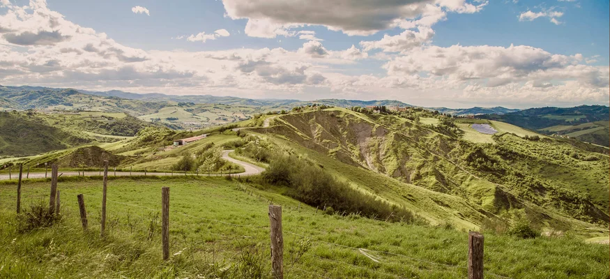 Grüne Hügel mit Zaun und bewölktem Himmel in ländlicher Landschaft