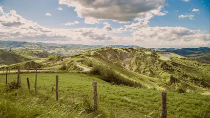 Grüne Hügel mit Zaun und bewölktem Himmel in ländlicher Landschaft