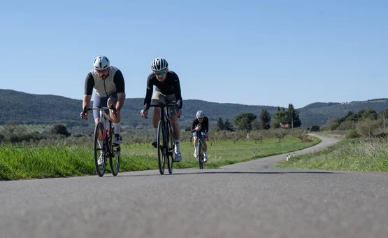 Gravelbike Urlaub in der Toskana © Mirrow Media Drei Radfahrer fahren auf einer Landstraße in ländlicher Gegend bei klarem Himmel.