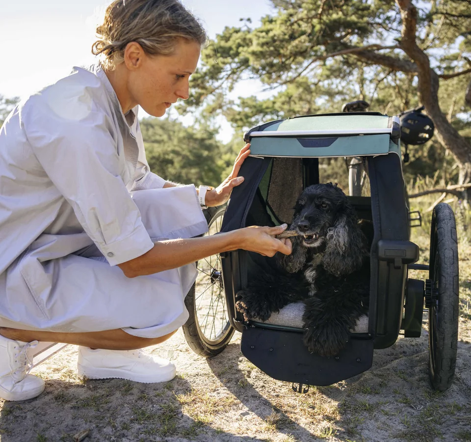 Mit dem Thule Bexey beginnt jedes Abenteuer zu zweit © Thule Eine Frau gibt einem Hund in einem Fahrradanhänger ein Leckerli