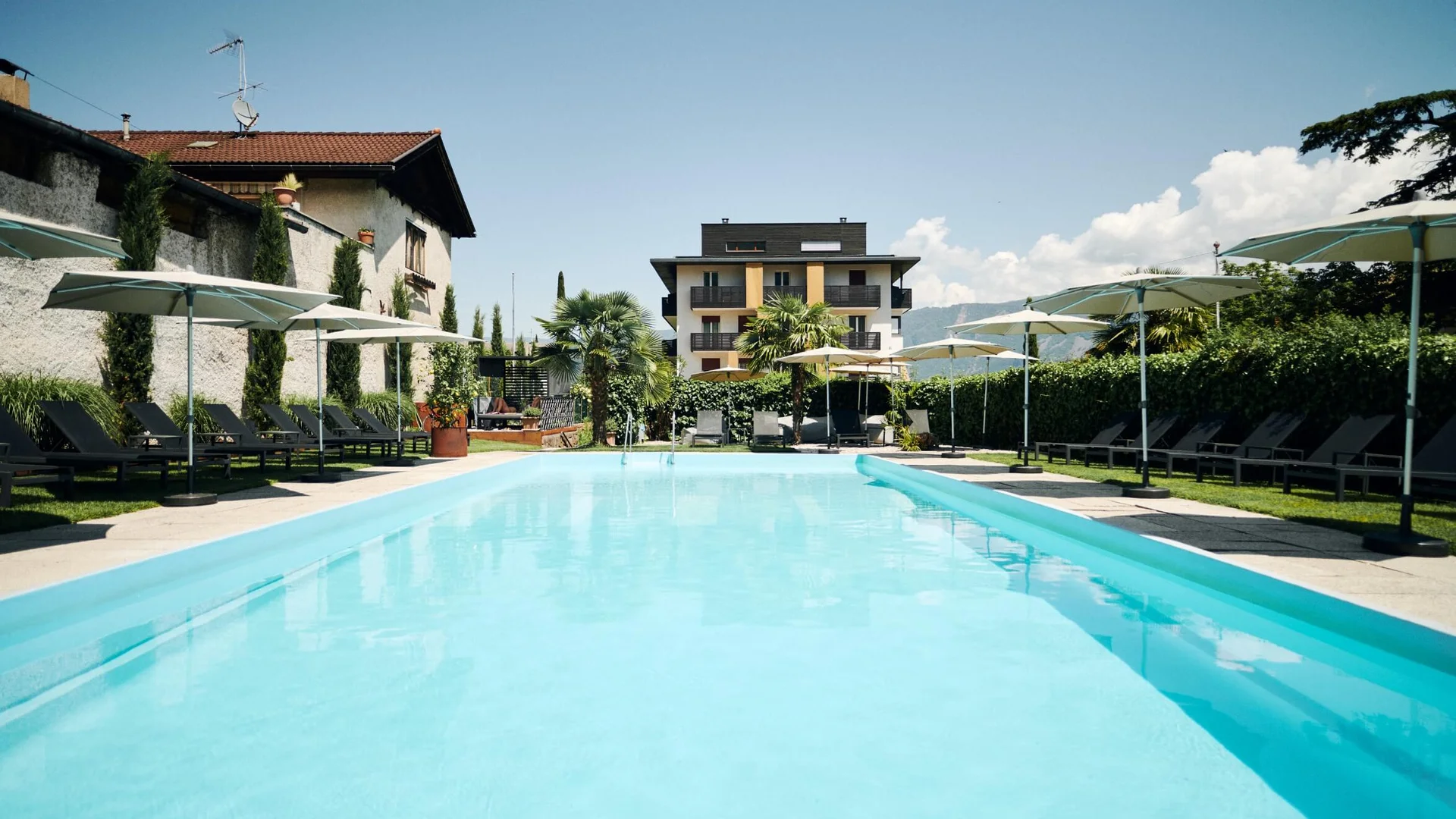Großer Pool mit Liegestühlen und Sonnenschirmen vor einem modernen Gebäude