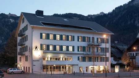 Müde Beine, volle Bäuche, offene Herzen © Hotel Bären - Cafe Deli Mellau Hotelgebäude mit beleuchteten Fenstern am Abend in bergiger Umgebung