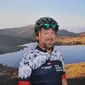 Mann mit Fahrradhelm vor Bergsee und Felsen im Hintergrund