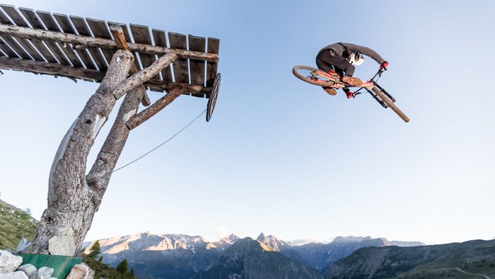 Mountainbiker macht einen Sprung von einer hölzernen Rampe in den Bergen