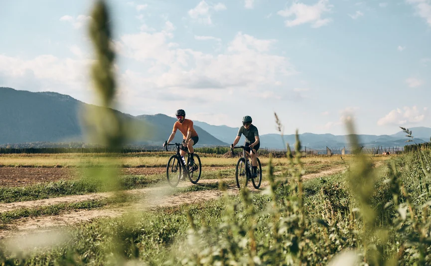 Zwei Radfahrer fahren auf einem ländlichen Weg mit Bergen im Hintergrund