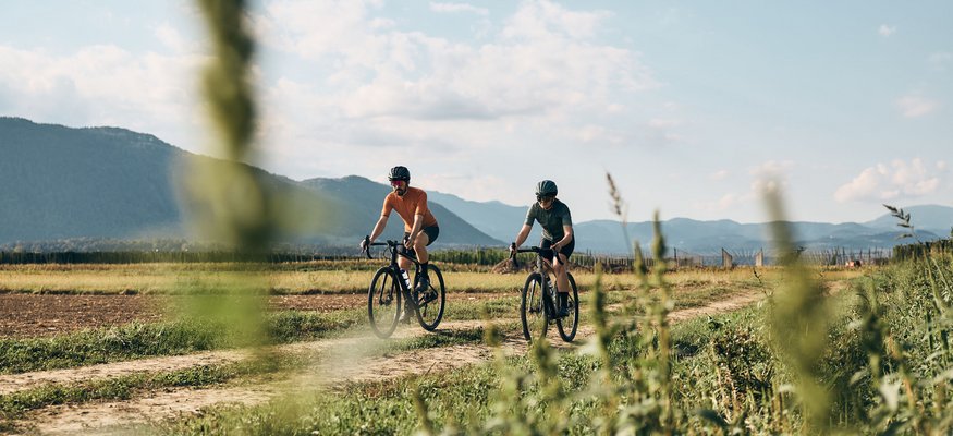 Zwei Radfahrer fahren auf einem ländlichen Weg mit Bergen im Hintergrund