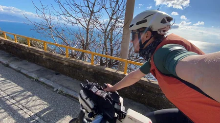 Bikepacking von Wien nach Athen © Jan Koller Fahrradfahrer mit Helm fährt an Meeresküste auf sonniger Straße
