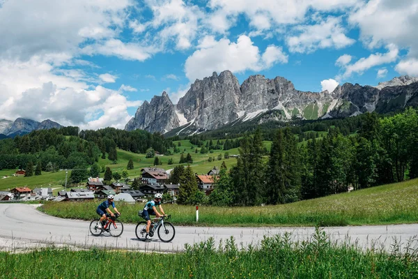 5 Gravelbike-Touren in Alta Badia, die du gefahren haben solltest © Hotel Melodia del Bosco Zwei Radfahrer fahren auf einer Straße mit Alpenbergen und grüner Landschaft im Hintergrund