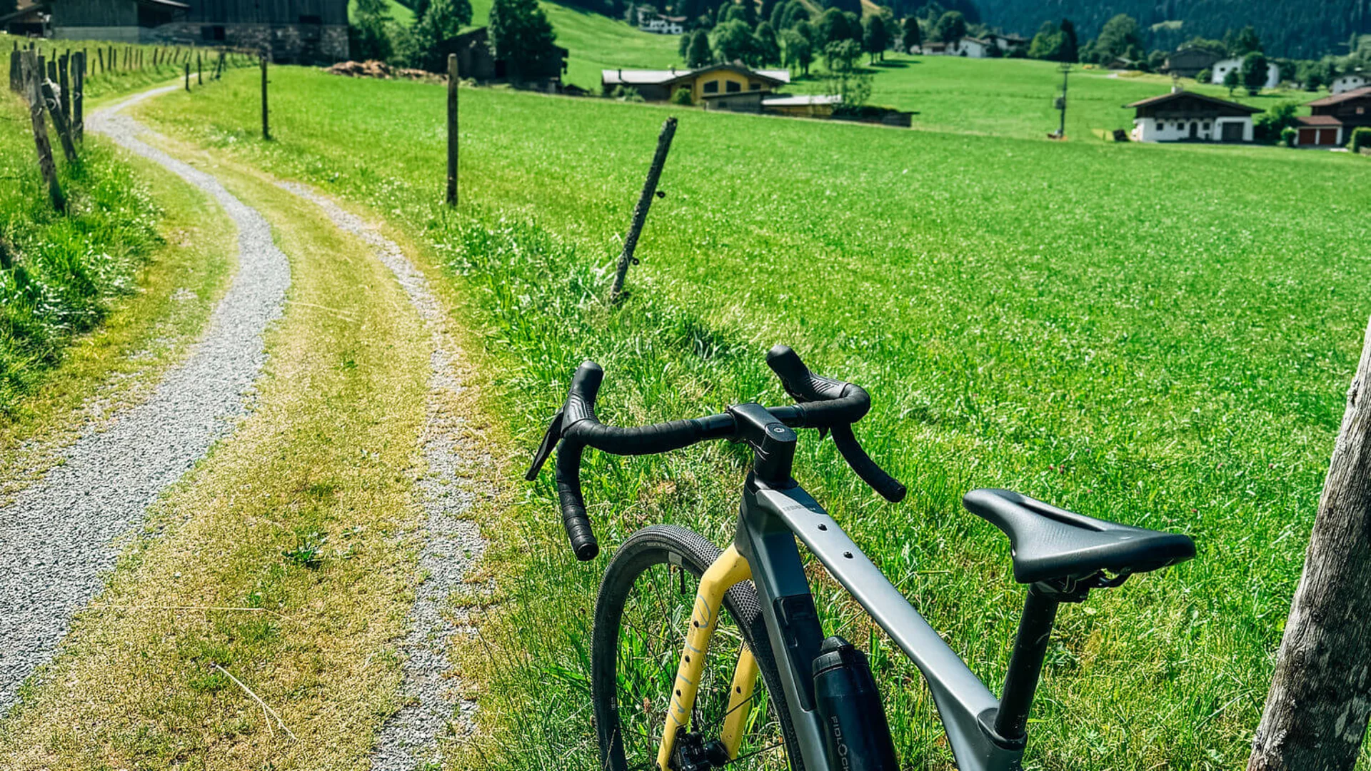 Graveln in den Kitzbüheler Alpen © Martina Wunderle / Flo Distl Fahrrad an Pfosten neben Feldweg in grüner Berglandschaft