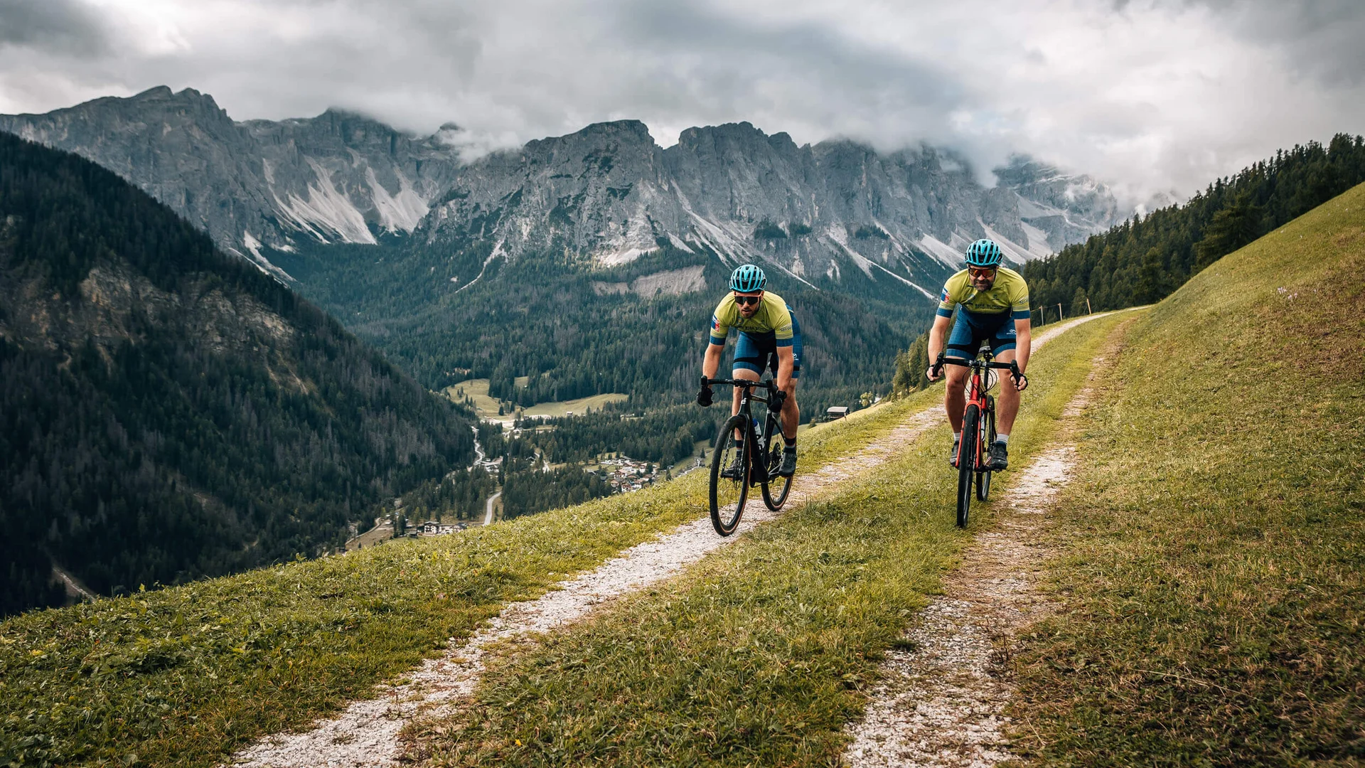 Zwei Radfahrer fahren auf einem Bergweg mit Alpen im Hintergrund