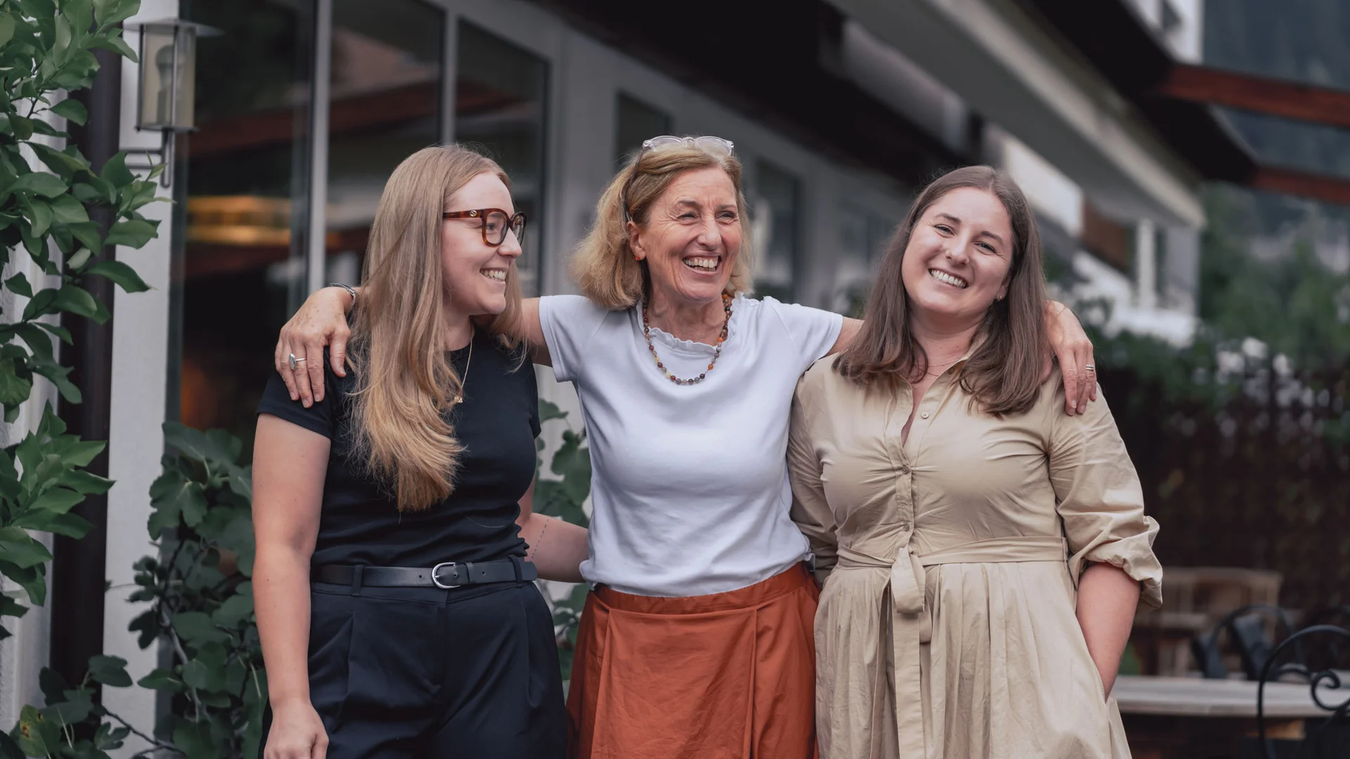 Three smiling women standing arm in arm outside a building