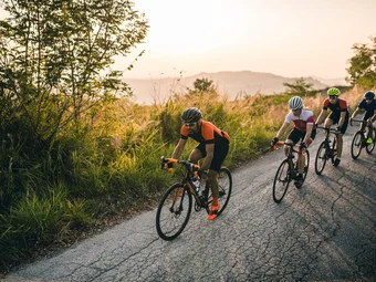 Emilia Romagna © Alex Moling Vier Radfahrer fahren auf einer Straße neben grüner Vegetation am Abend