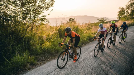 Four cyclists riding on a road beside greenery at sunset