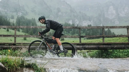 Radfahrer fährt mit Mountainbike durch Bach in bergiger Landschaft